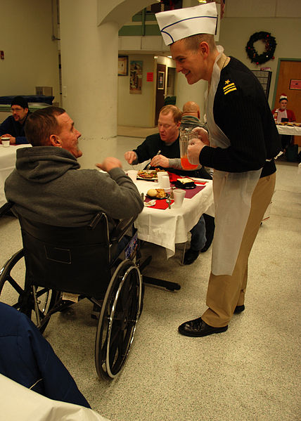 Lt. Cmdr. Anthony Savage chats with a veteran at the New England Center for Homeless Veterans during a Christmas dinner visit.
